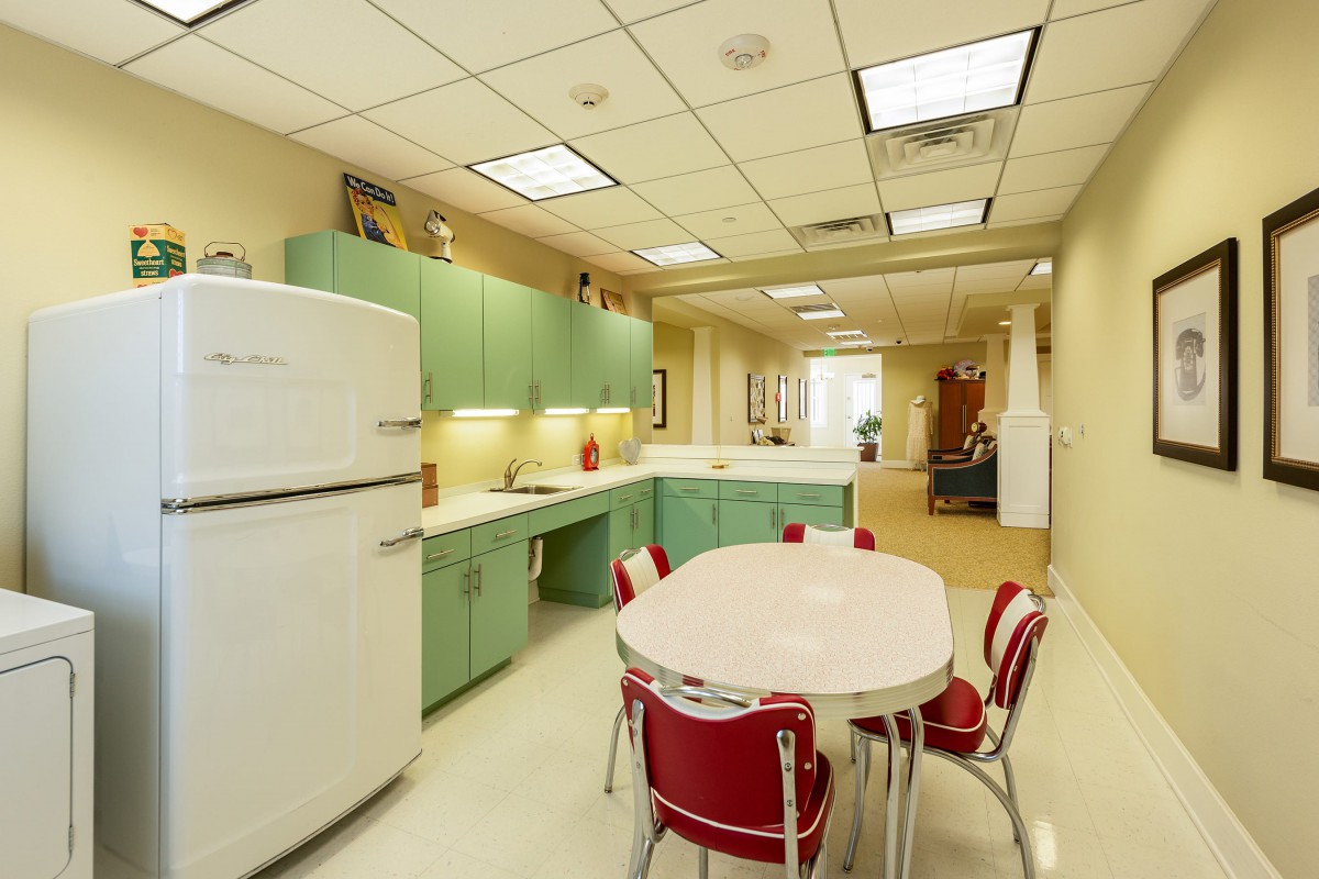 A retro-style kitchen with pastel green cabinets, a vintage refrigerator, and a dining table with red chairs.