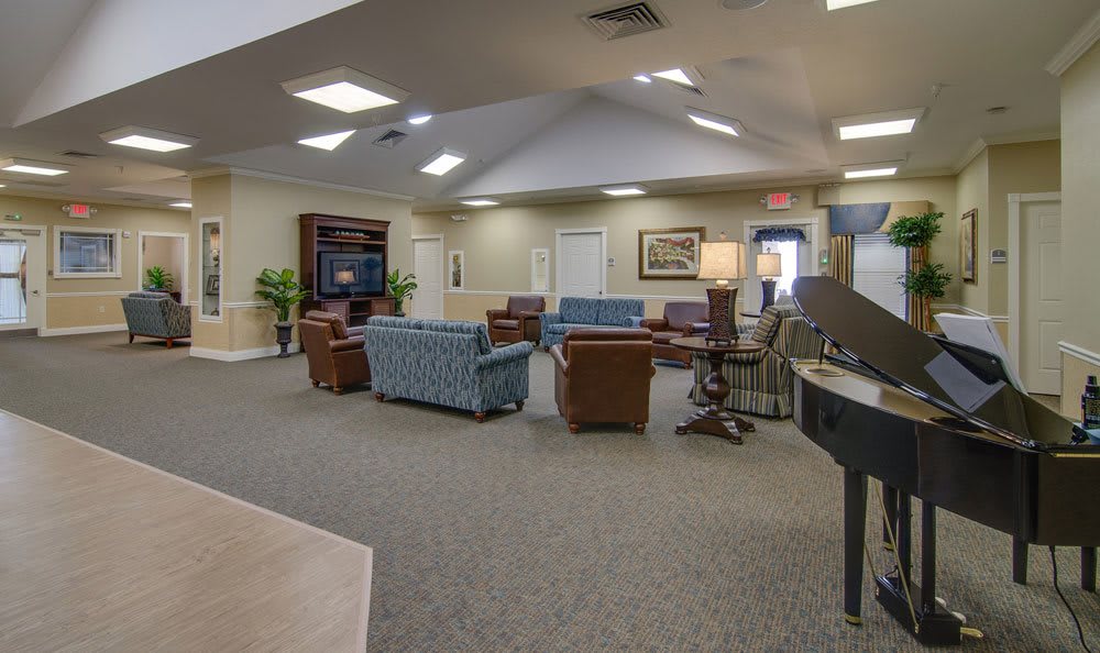 A spacious living room area with assorted furniture, including sofas, chairs, a piano, and a television.