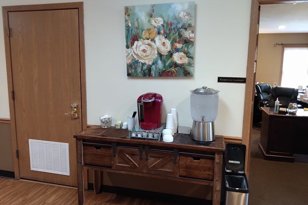 A cozy refreshment station with a coffee machine, water dispenser, and floral artwork.