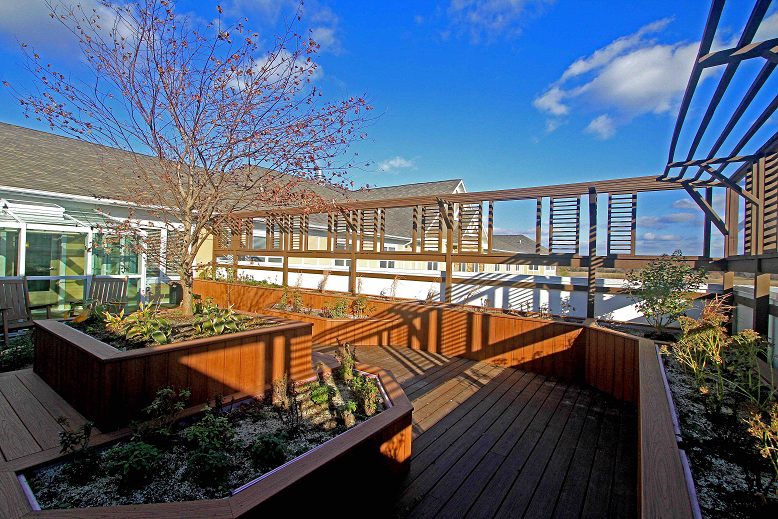 A sunny rooftop deck with wooden structures and plants under a clear blue sky.