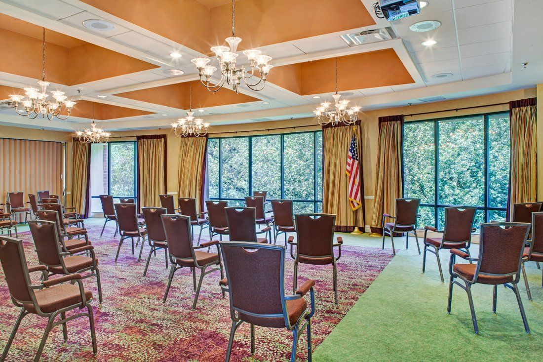 An elegant conference room with arranged chairs, large windows, and chandeliers.
