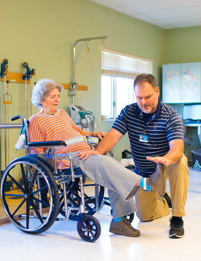 A therapist is assisting an elderly patient in a wheelchair during a physical therapy session.