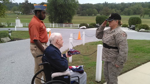 A veteran in a wheelchair receives honors from a service member during a ceremony.