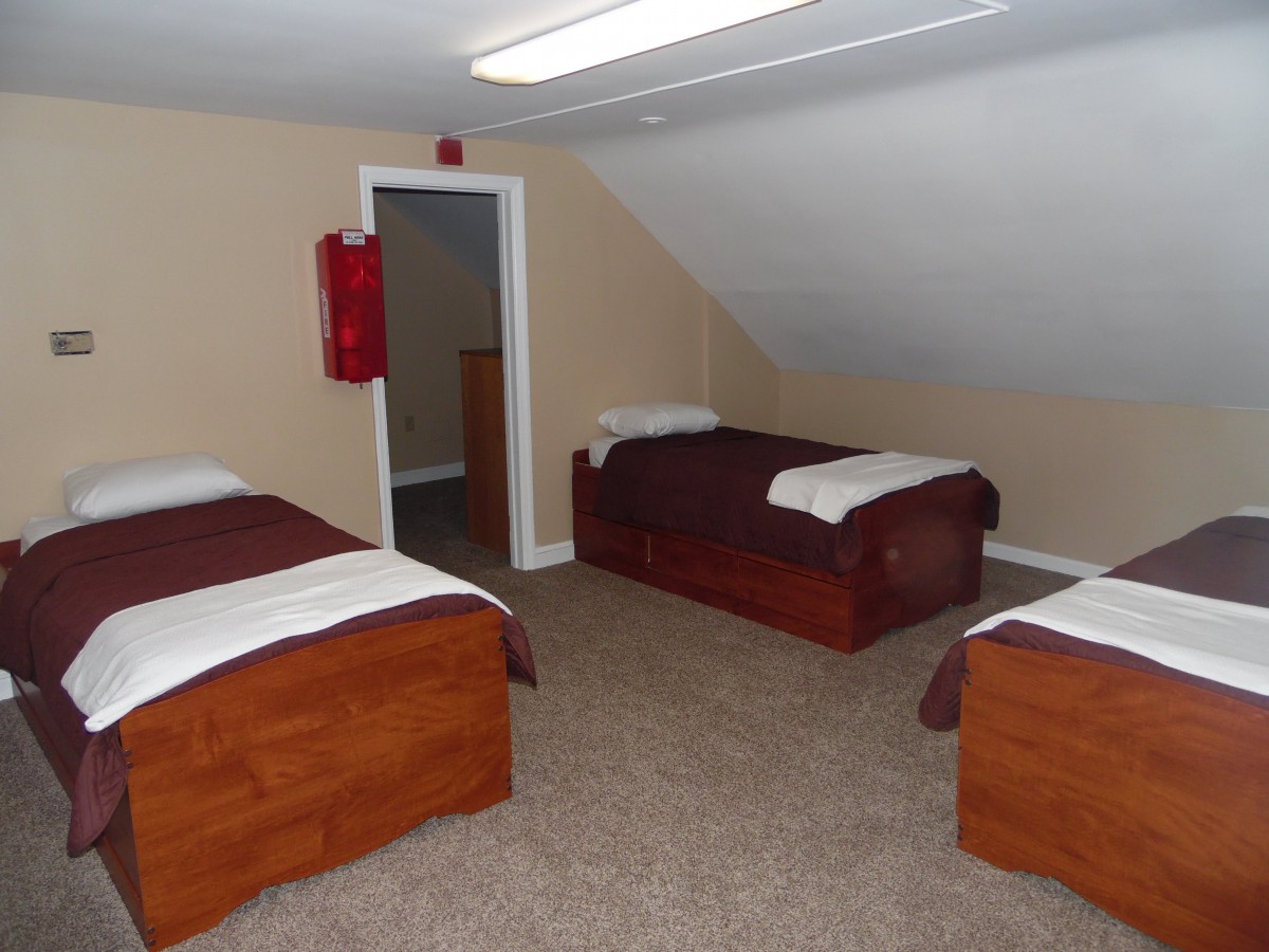 A simple attic bedroom with three single beds and a carpeted floor.