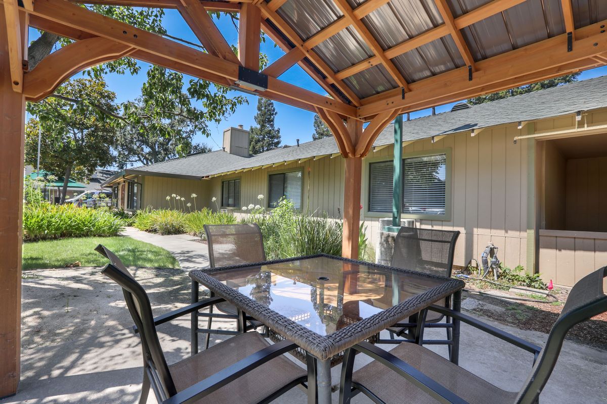 A sunny patio with outdoor seating beneath a wooden pergola.
