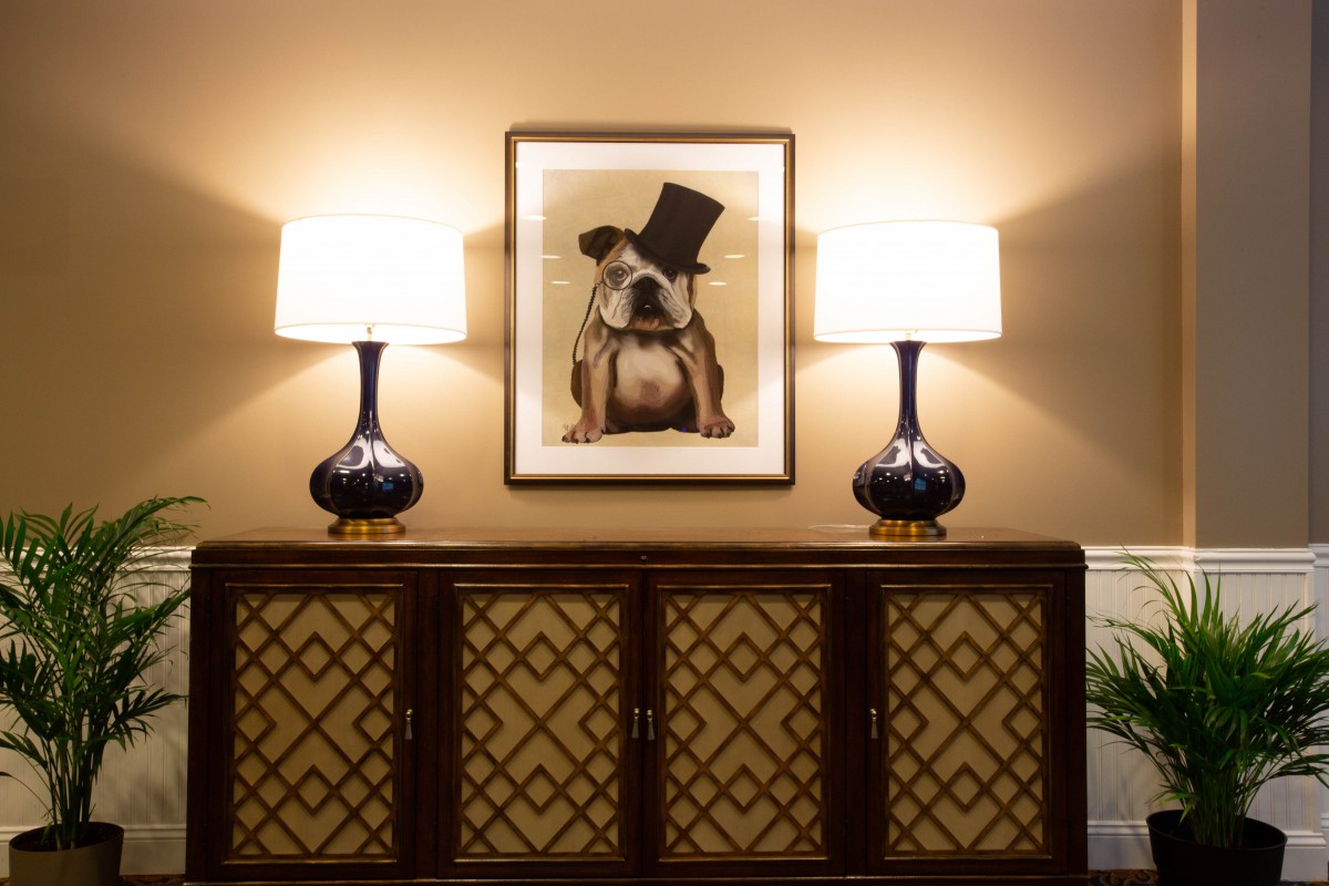 A stylish room with a dog portrait and two table lamps on a cabinet.
