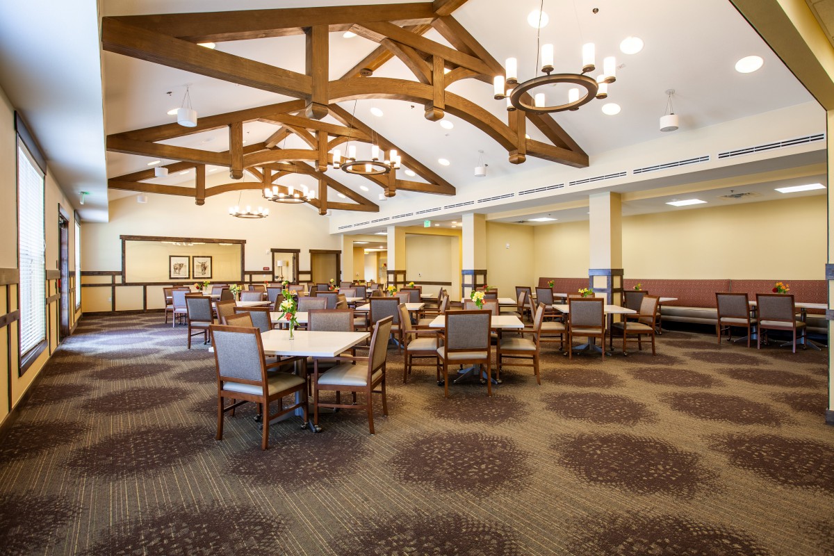 A spacious dining area with multiple tables and chairs, adorned with chandeliers and wooden beams.