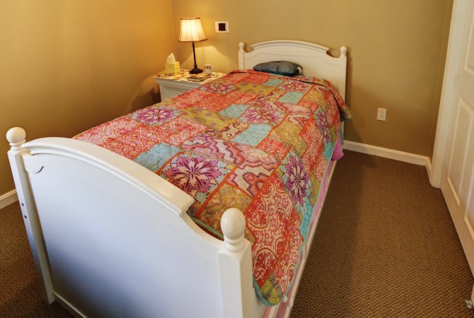 A cozy bedroom with a single bed featuring a colorful quilt and a bedside lamp on the nightstand.
