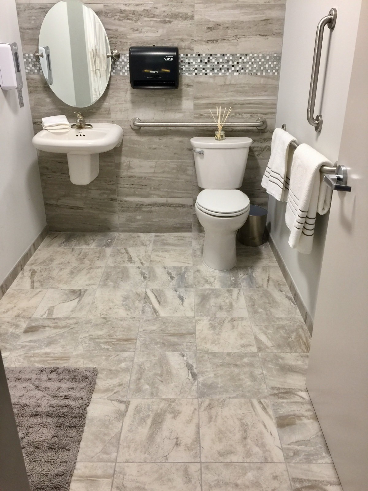 A modern bathroom with a toilet, sink, and mirror, featuring tiled flooring and neatly arranged towels.
