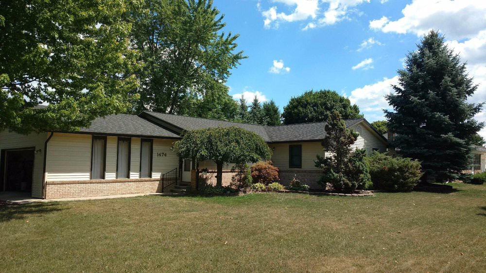 A suburban house with a well-maintained lawn and trees under a blue sky.
