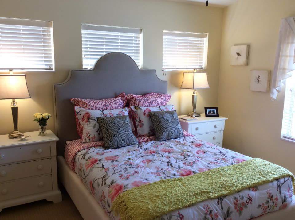 A cozy bedroom featuring a bed with floral bedding and multiple pillows, flanked by nightstands with lamps.