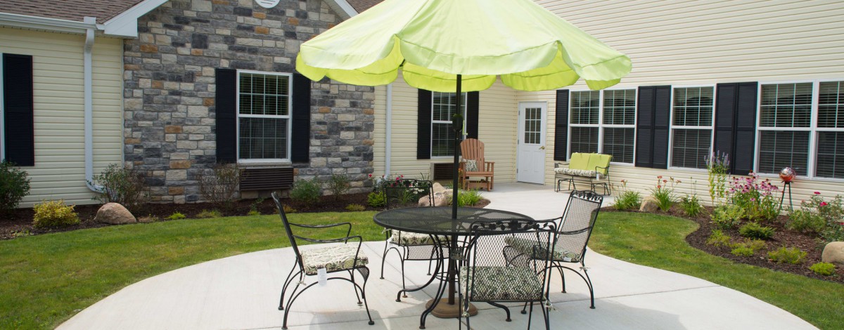 A cozy backyard patio with a table, chairs, and a green umbrella.