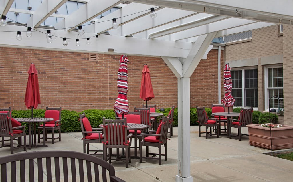 A patio with red-cushioned chairs and tables under a pergola adorned with string lights.
