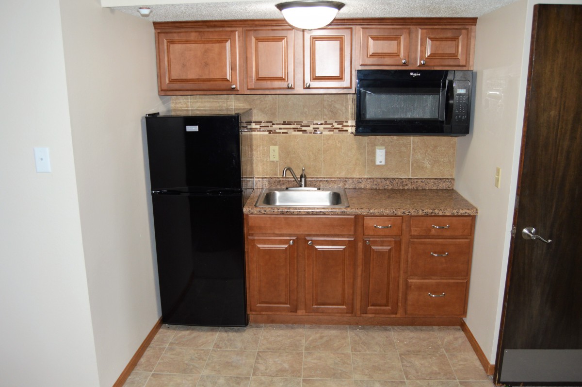 A compact kitchen space with a fridge, microwave, sink, and wooden cabinets.