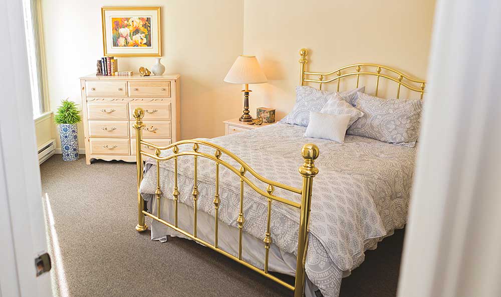 A cozy bedroom with a brass bed, dresser, and a lamp creating a warm atmosphere.