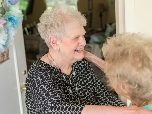 An elderly woman smiling and embracing another person indoors.