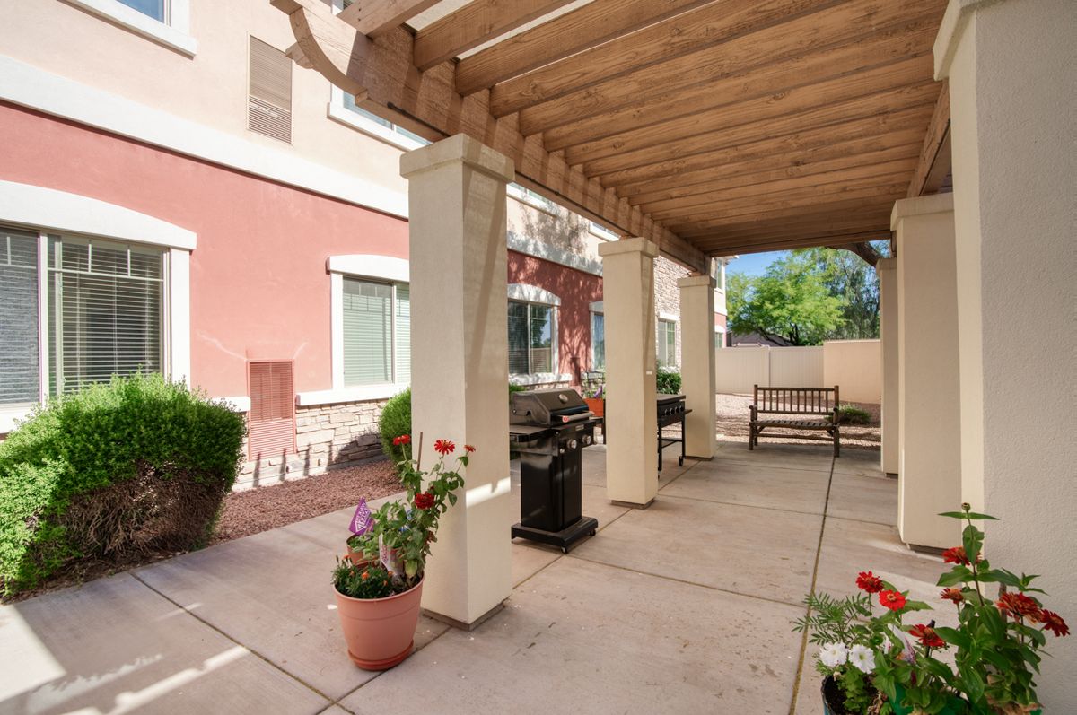 A cozy outdoor patio with a pergola, featuring potted flowers, a bench, and a grill.