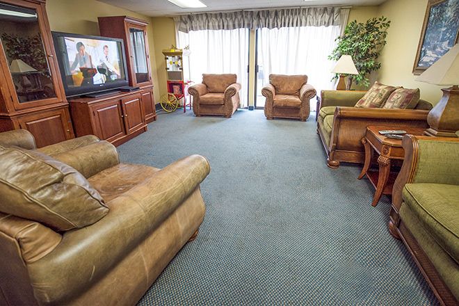 A cozy living room with multiple armchairs, a sofa, a television, and a large window with curtains.