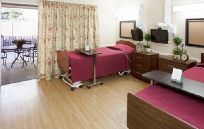 A hospital room with two patient beds, medical equipment, and floral curtains.