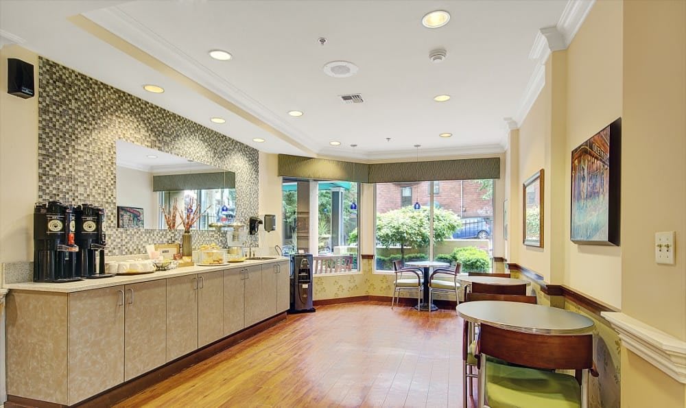 A cozy cafe interior with a beverage station and seating, featuring modern decor and large windows.