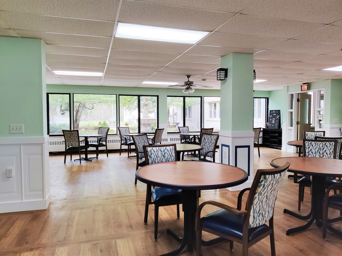 A spacious dining area with several tables and chairs, featuring large windows allowing natural light.