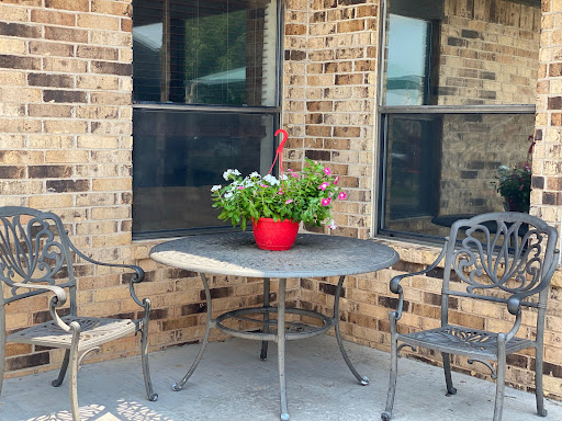 A cozy outdoor seating area featuring a table, chairs, and a vibrant flower arrangement in a red pot.