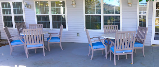 A cozy outdoor patio area featuring wooden chairs with blue cushions and a couple of tables, perfect for relaxation.