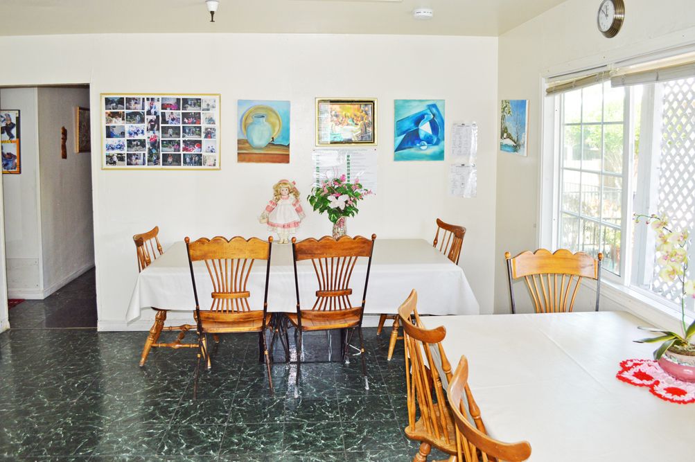 A cozy dining area with wooden chairs and tables, decorated with artwork and a flower arrangement.
