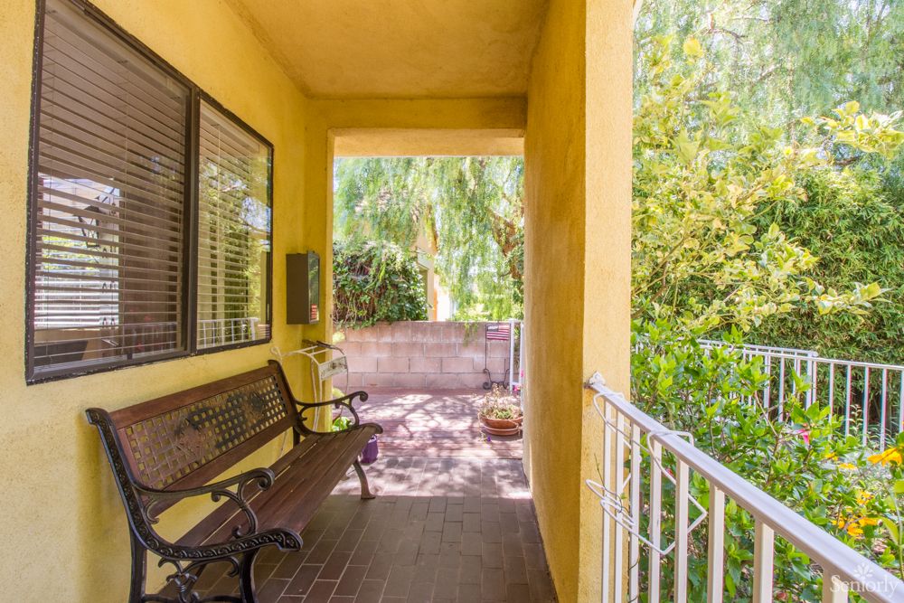 A charming porch with a garden view featuring a wooden bench and yellow walls.