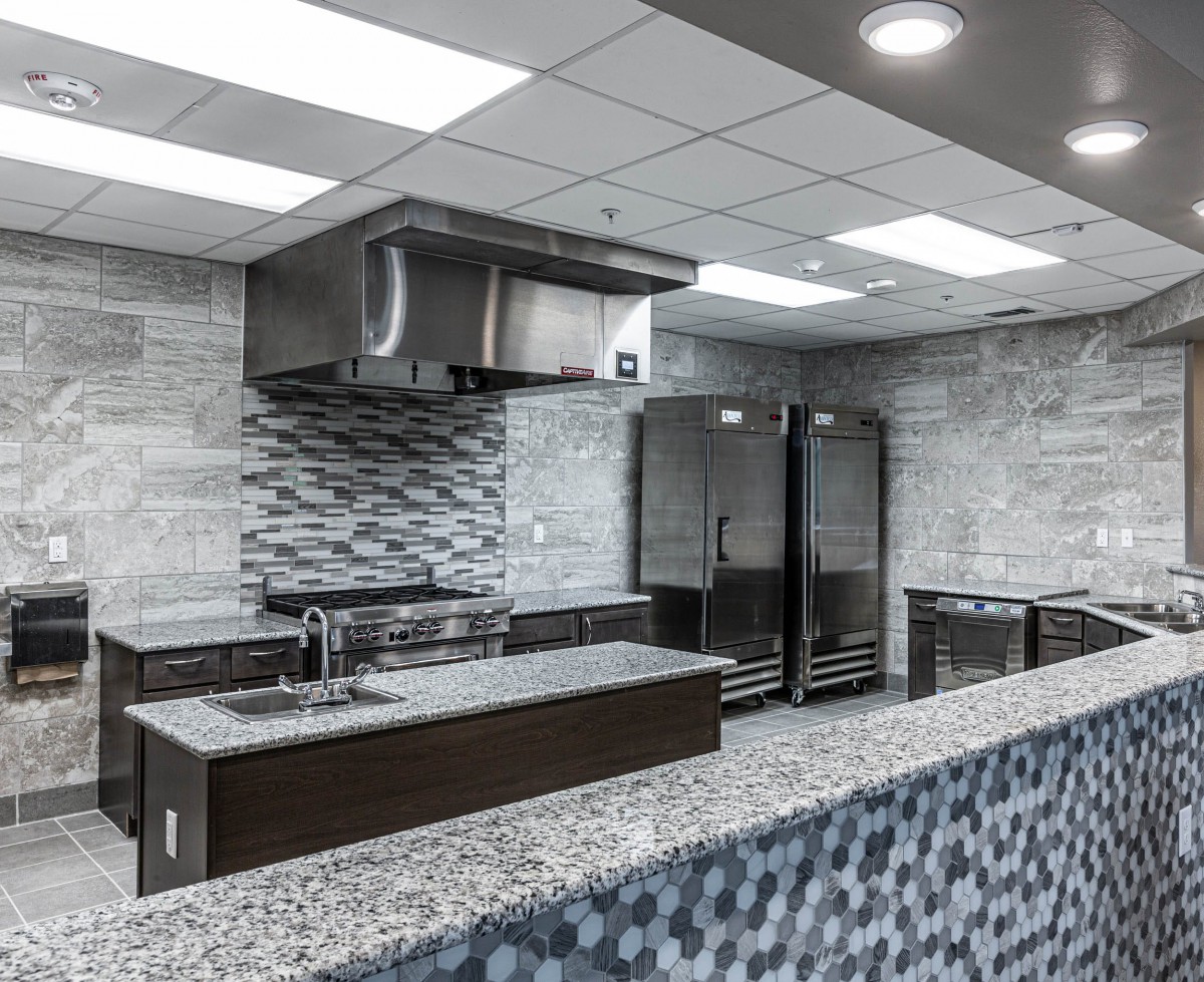 A modern commercial kitchen with stainless steel appliances, a tile backsplash, and a granite countertop.