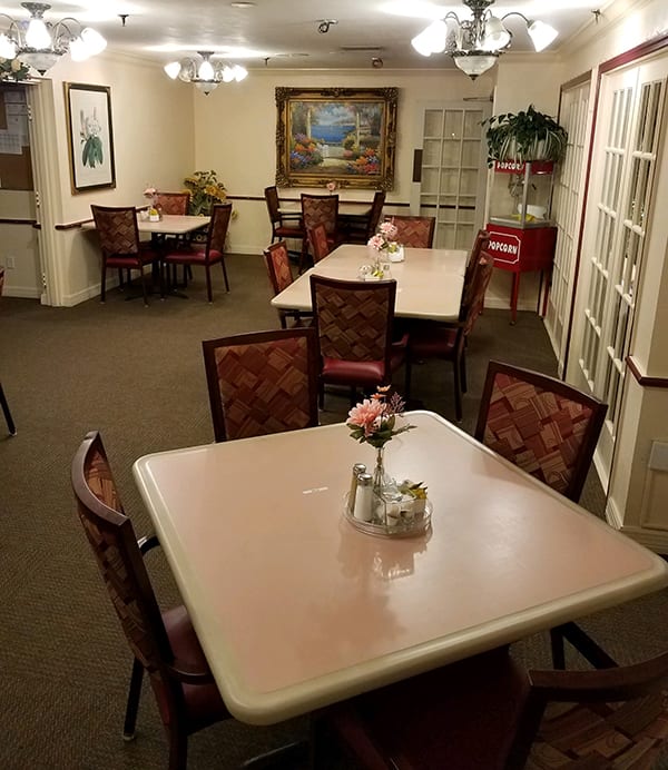 A well-lit dining area with multiple tables and chairs, adorned with paintings and plants, creating a cozy atmosphere.