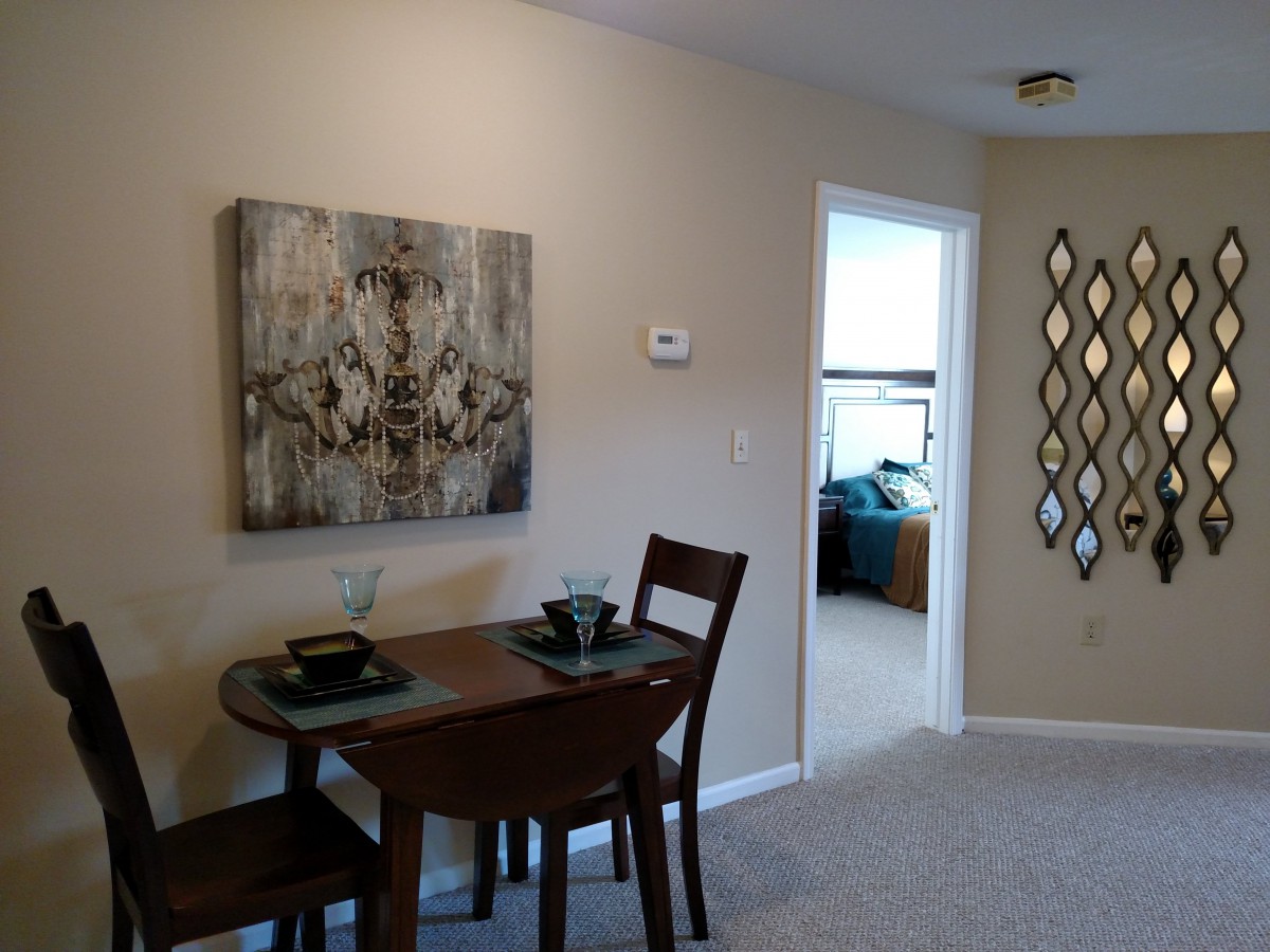 A small dining area featuring a table set with two chairs, adorned with artwork on the wall and a decorative mirror.