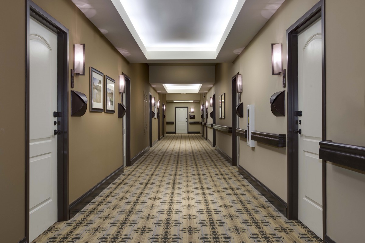 A well-lit hotel hallway with patterned carpet and multiple doors on either side.