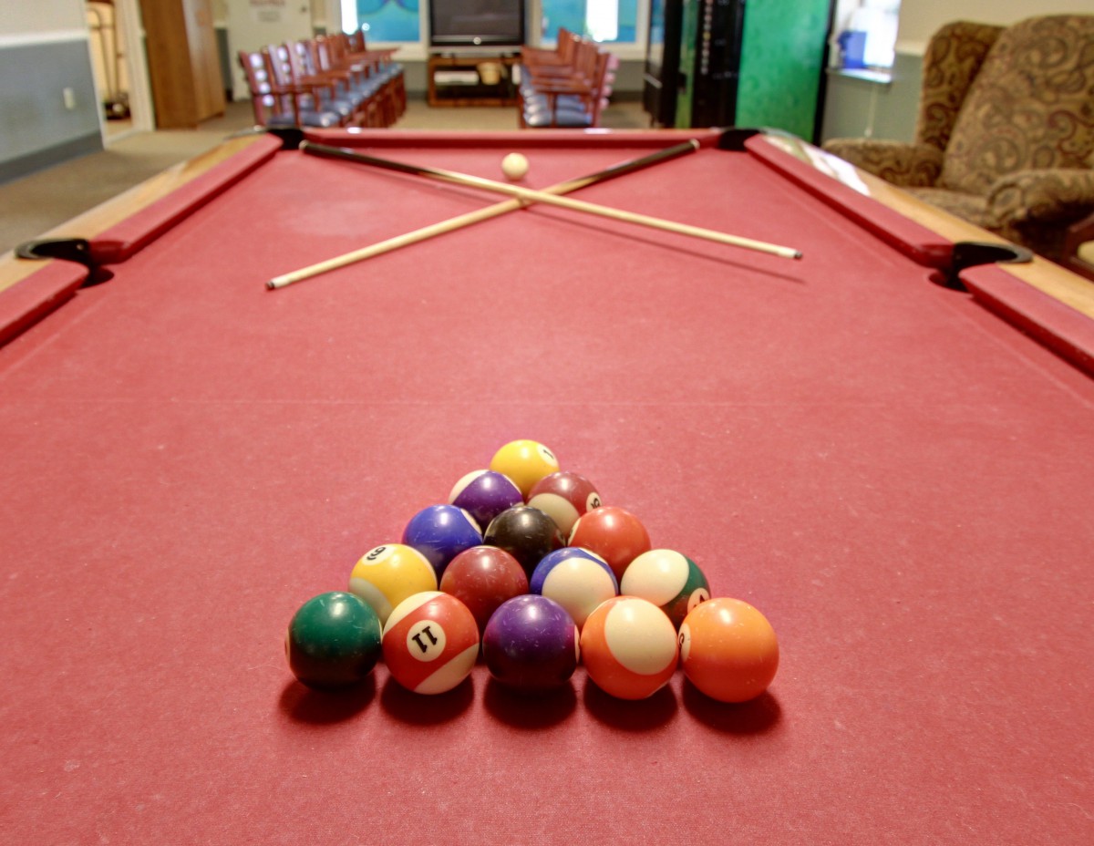A billiards setup with pool balls racked and cues on a red pool table in a game room.