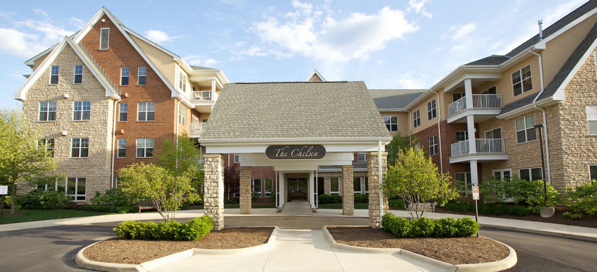 A well-maintained residential building entrance with stone pillars and clear skies.