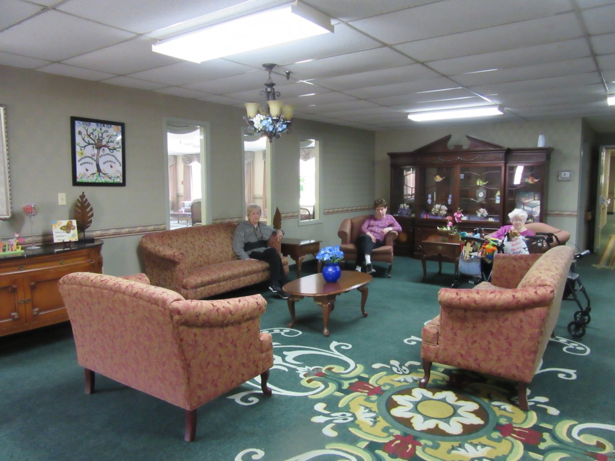 A cozy living room with sofas, chairs, and a chandelier, where several people are seated.