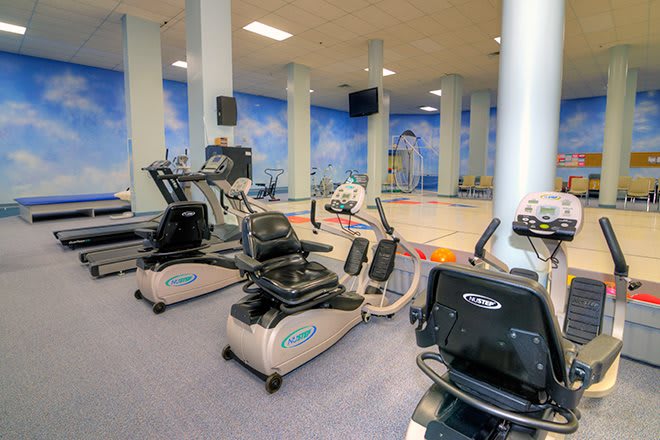 A fitness center with various exercise equipment including treadmills, set in a bright and spacious environment.