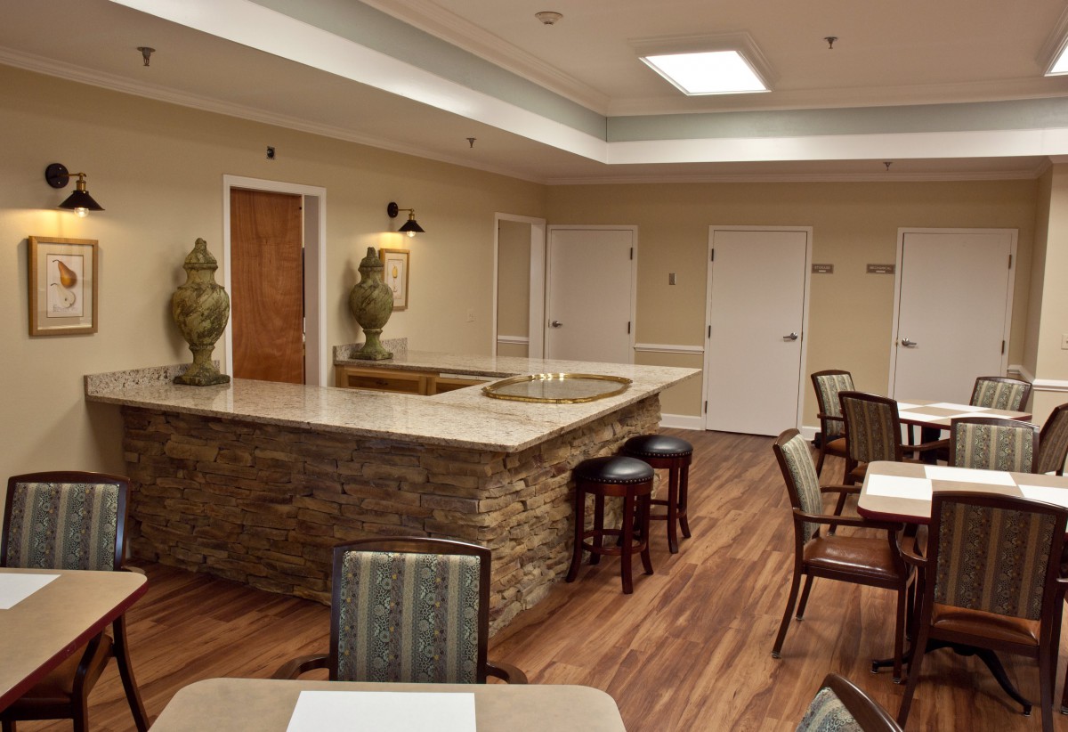 A modern reception area with seating and bar stools, featuring wood flooring and ambient lighting.