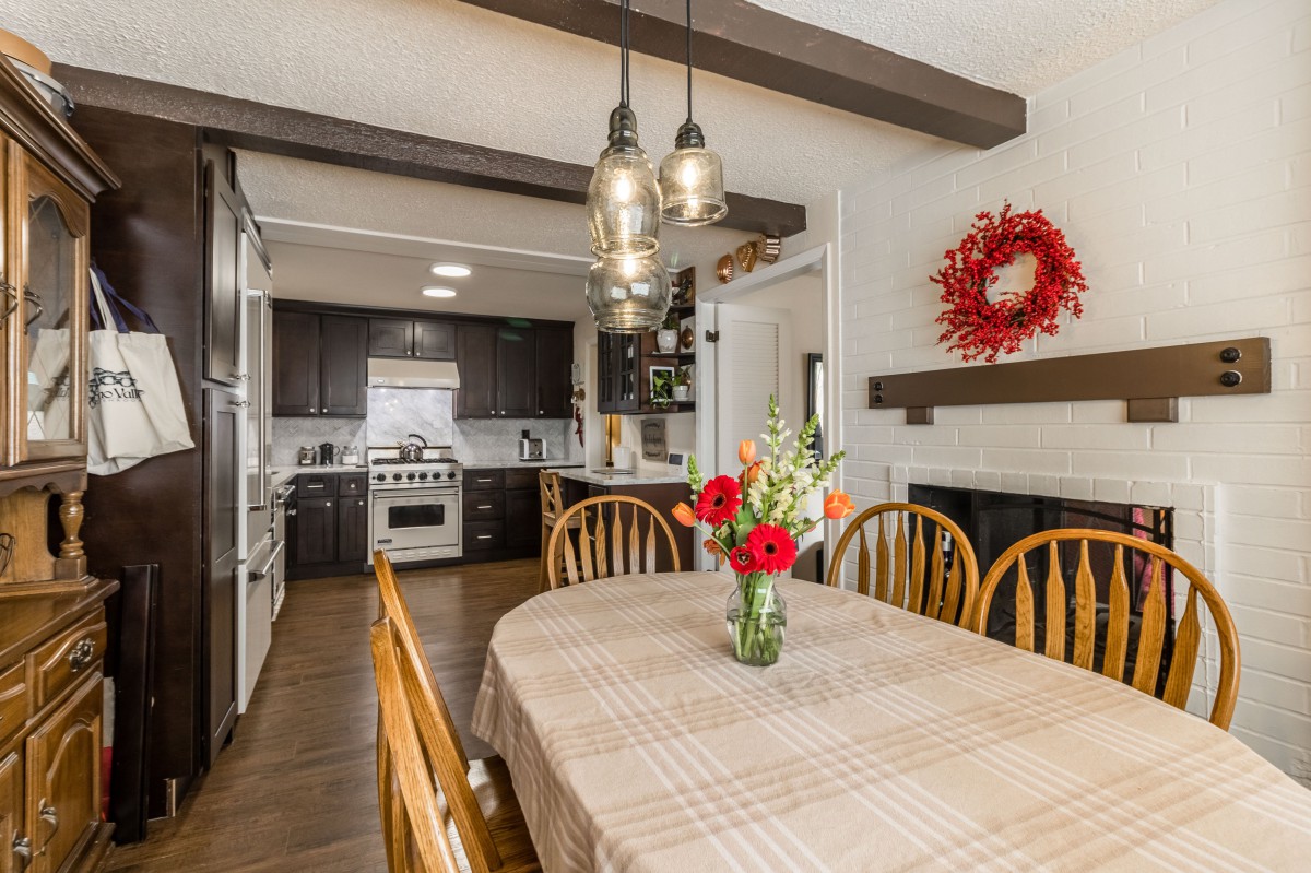 A cozy kitchen-dining area with a wooden table, adorned with flowers and illuminated by pendant lights.