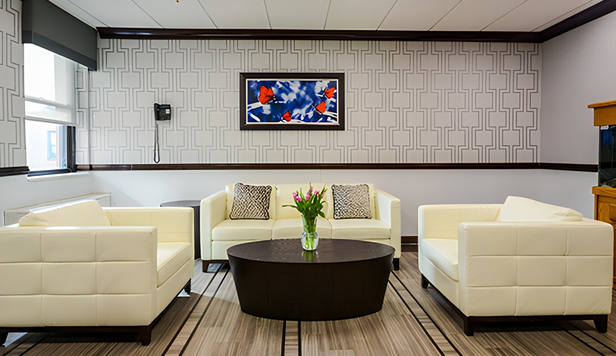 A modern living room featuring white sofas, a dark oval coffee table, and decorative artwork on the wall.