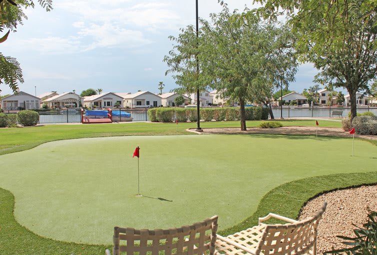A serene golf putting green overlooking a lake with benches and nearby residential homes.