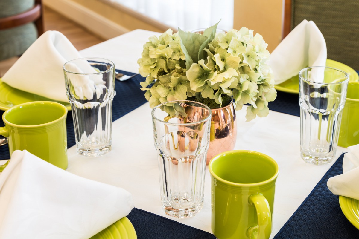 A neatly arranged dining table with a floral centerpiece and bright green mugs.