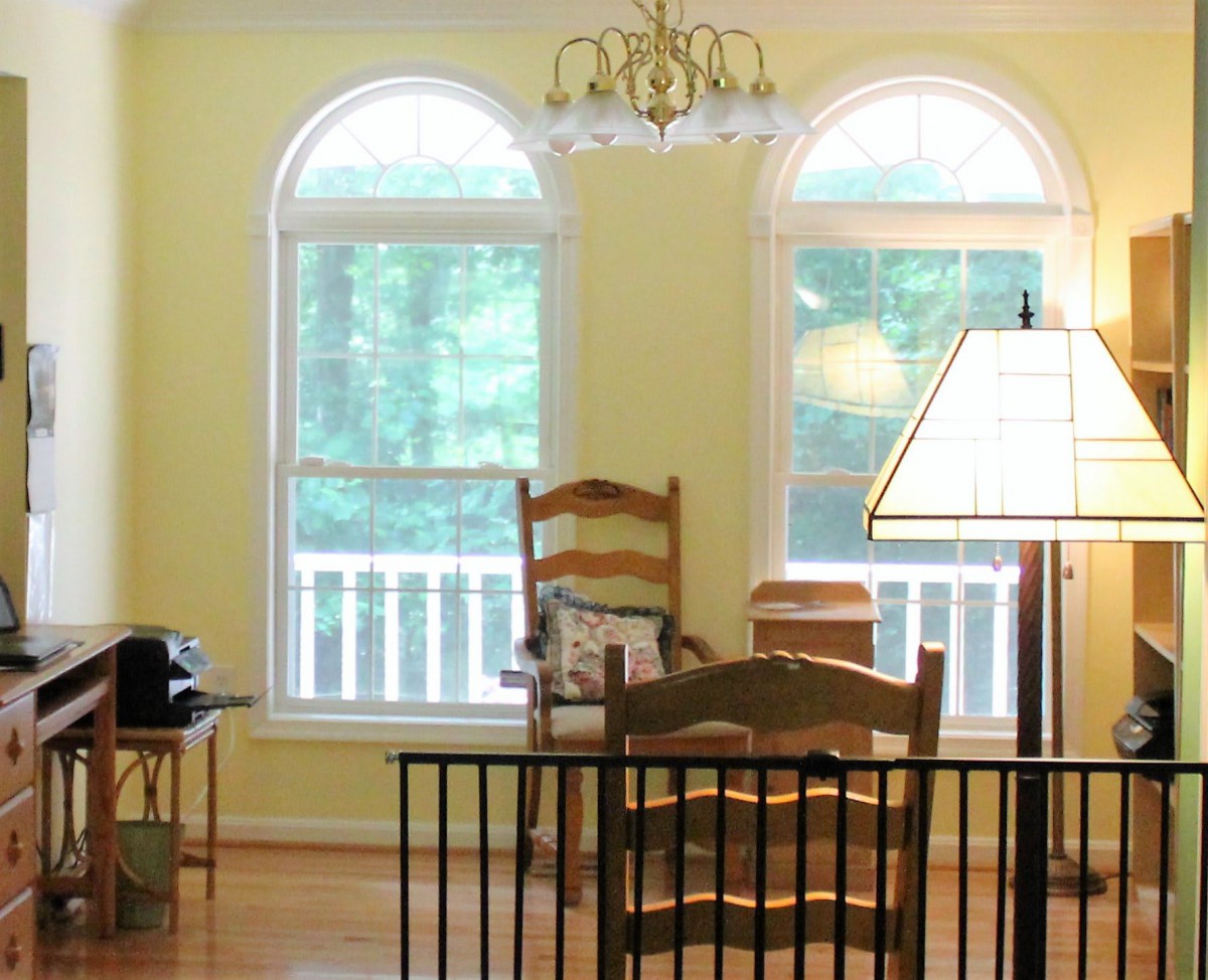 A cozy interior featuring wooden chairs and a lamp by two large arched windows.