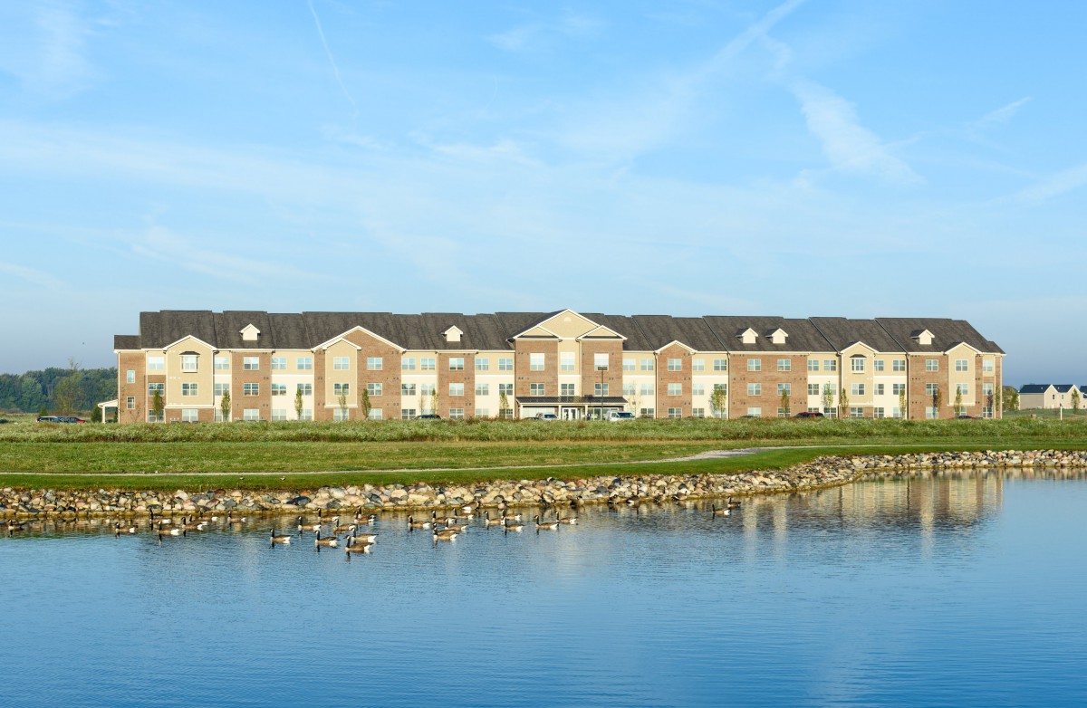 A large building with a scenic view across a pond, where geese are seen on the water.