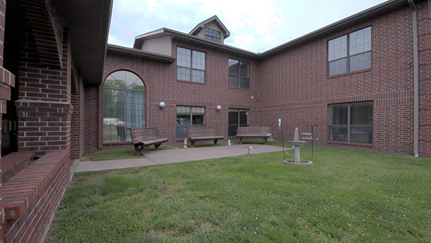 A courtyard with grass, benches, and a brick building in the background.