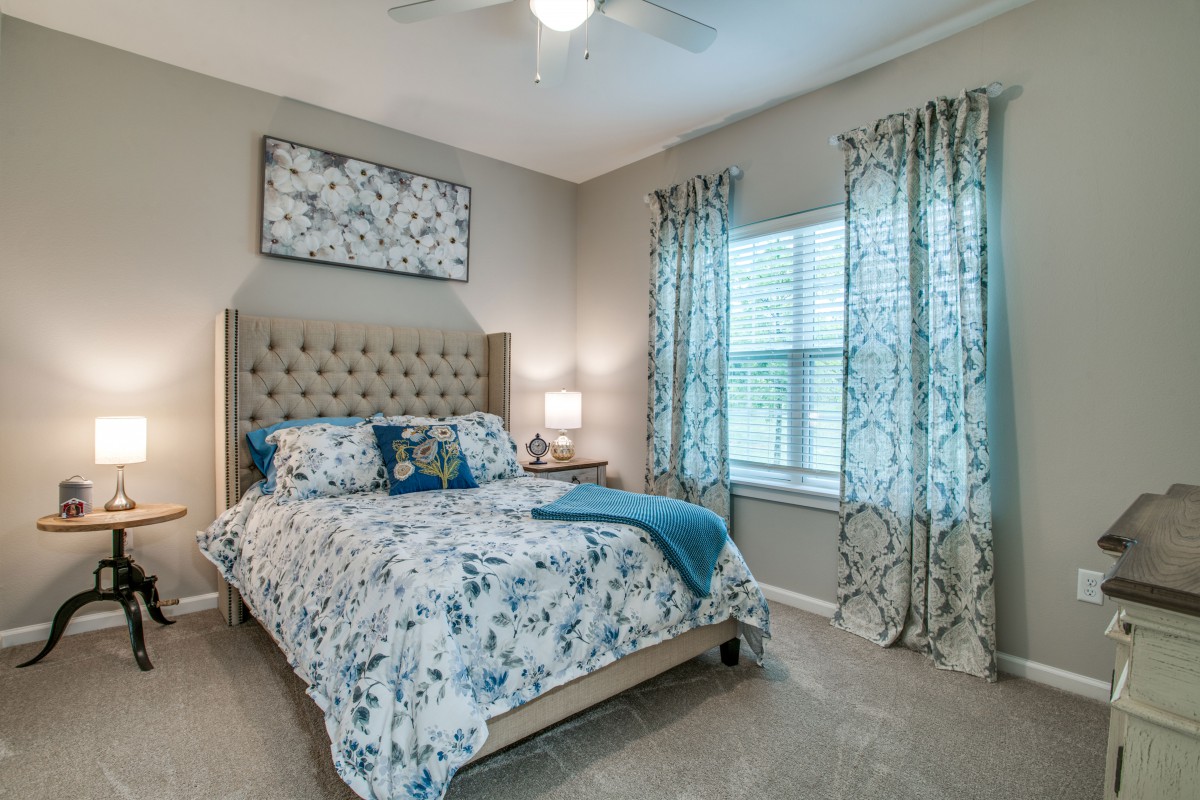 A cozy bedroom with floral bedding and matching curtains, featuring a lamp on the bedside table.