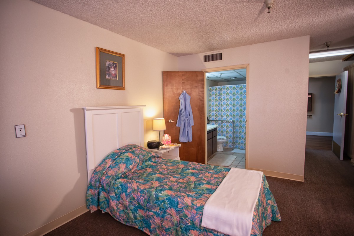 A cozy bedroom with a colorful bedspread, nightstand, and a view into the bathroom.