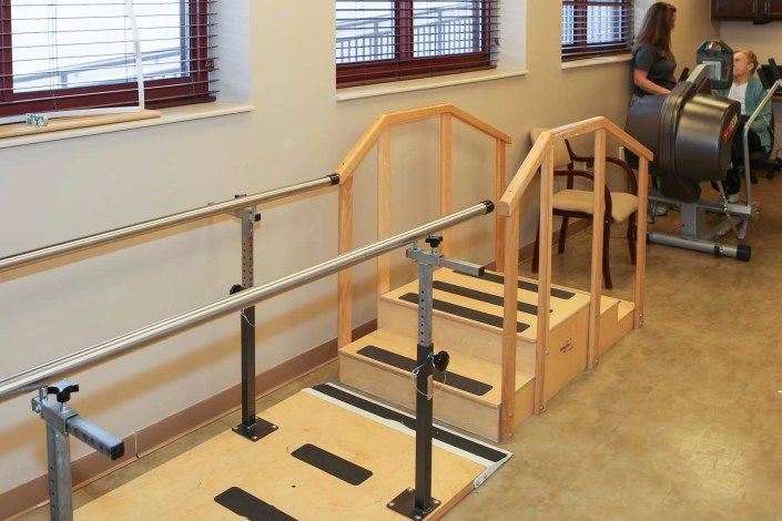Indoor rehabilitation area featuring parallel bars and stairs for physical therapy exercises.