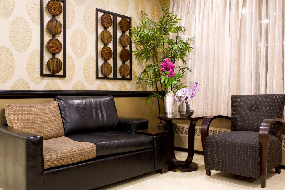 A cozy living room with modern furniture, featuring a dark sofa, an armchair, a coffee table with floral arrangements, and artistic wall decor.