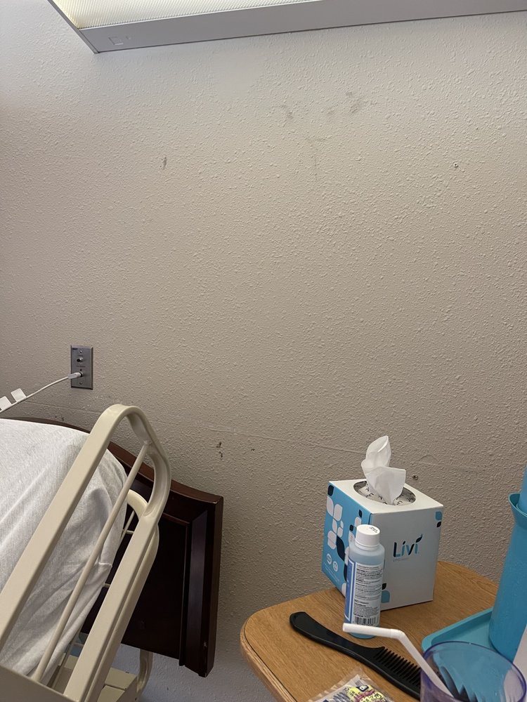 A hospital room with a bed and bedside table holding tissues and sanitizer.